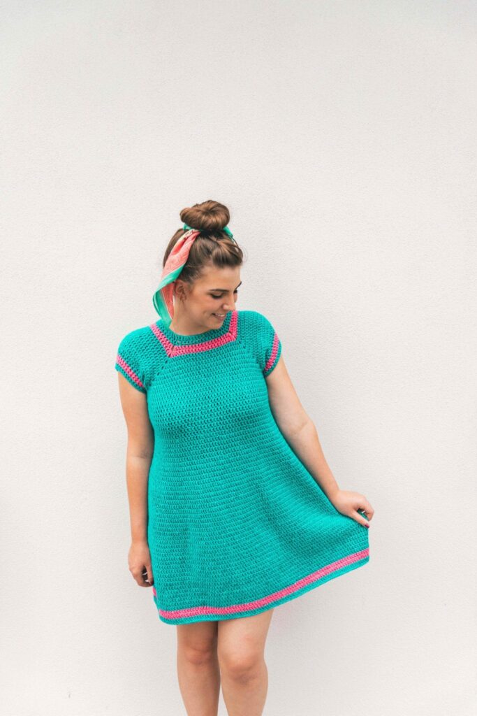 woman with a hair bun wearing a crochet teal dress with pink highlights