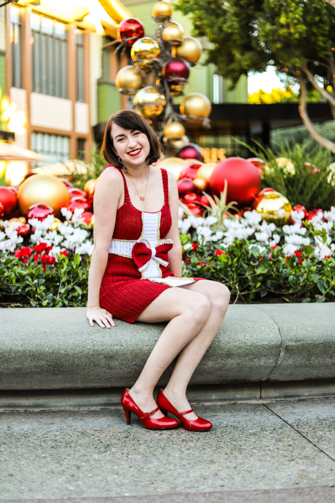 woman seated wearing a Holidays-inspired crochet dress with a large bow at the waist