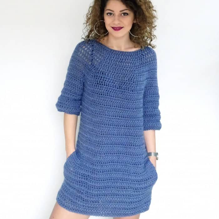 curly woman wearing a blue crochet dress with pockets