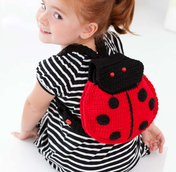 a little girl wearing the Red Heart Lady Bug Crochet Backpack